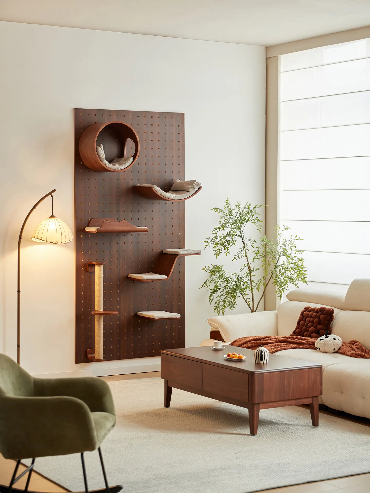 Walnut-finish pegboard cat wall with a circular den, cushioned perches and scratching post beside a living-room sofa